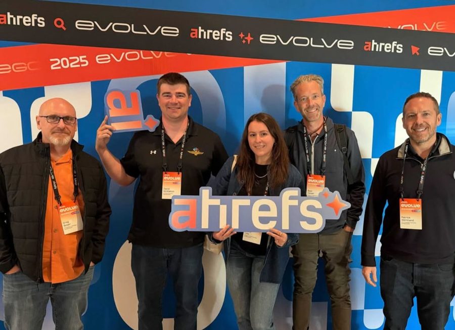 Five attendees wearing lanyards in front of an Ahrefs sign at Ahrefs Evolve 2025.