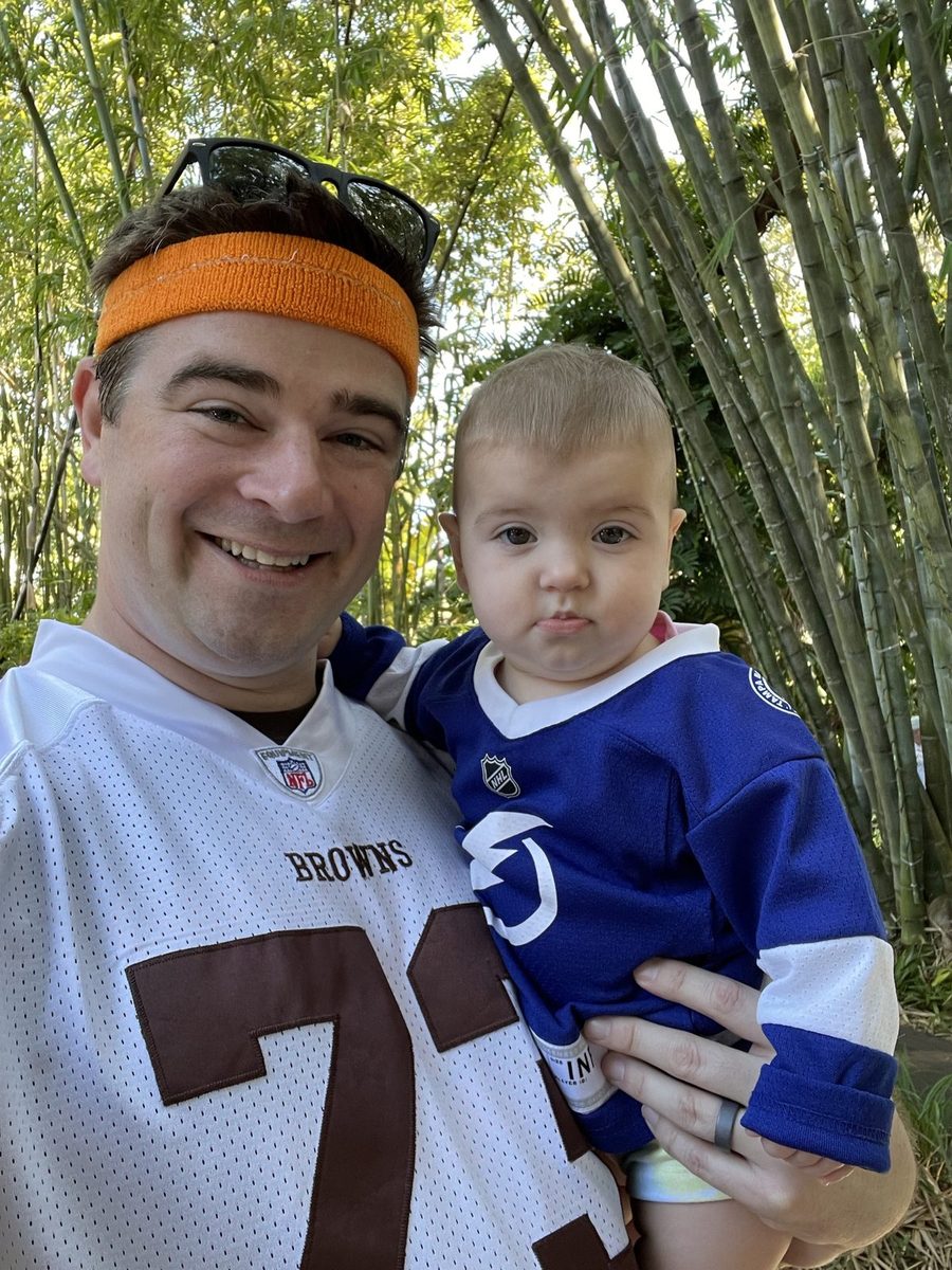 David McMahon in an orange headband and Browns jersey holding his young daughter Lily in a bamboo garden.