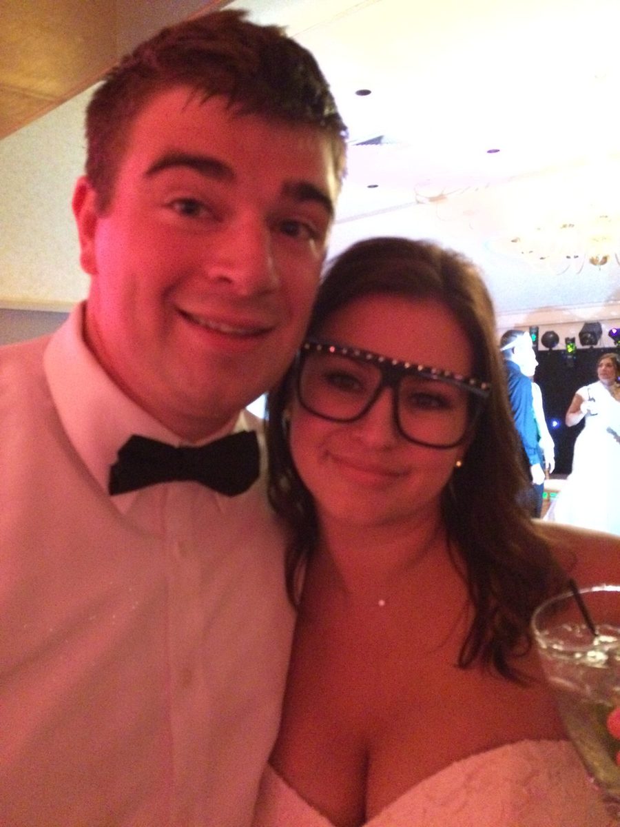 A man in a bow tie and a woman in studded glasses smiling at a wedding reception.
