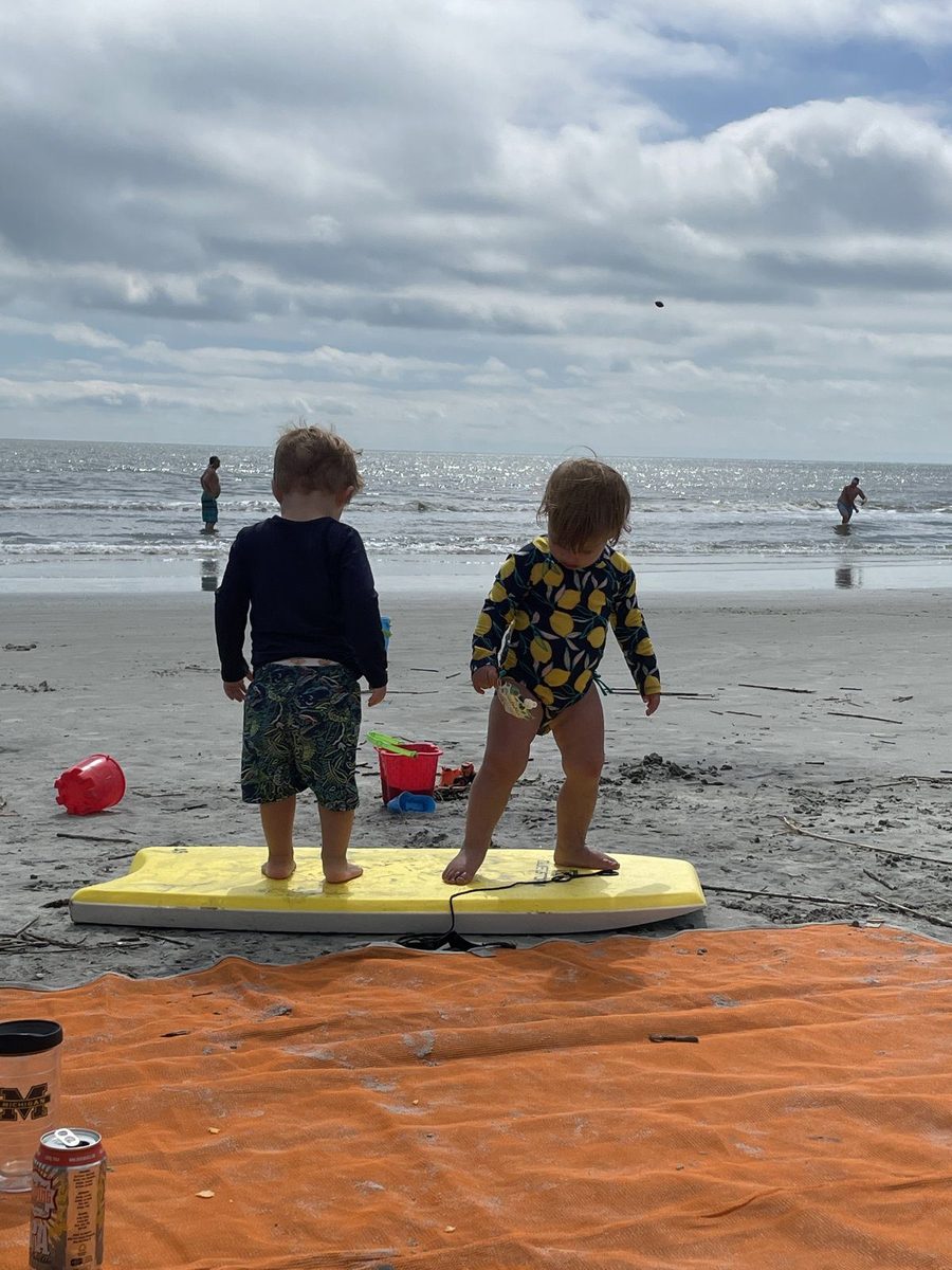Two toddlers standing on a yellow bodyboard on the beach at Hilton Head.
