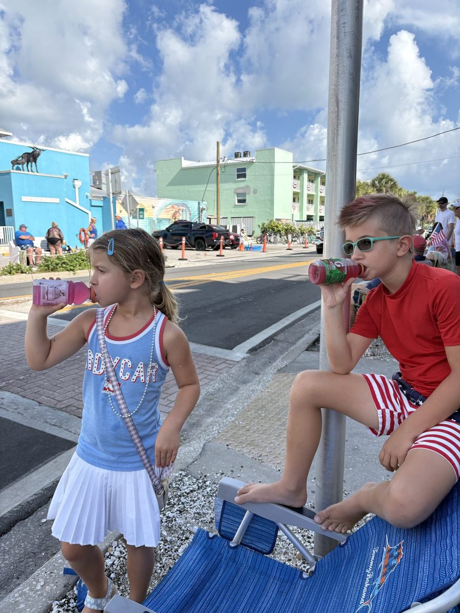 A girl and a boy drinking from cups while watching a parade on Anna Maria Island.