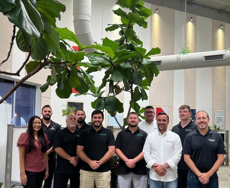 A group of NetReputation team members posing together in an office with a large plant.