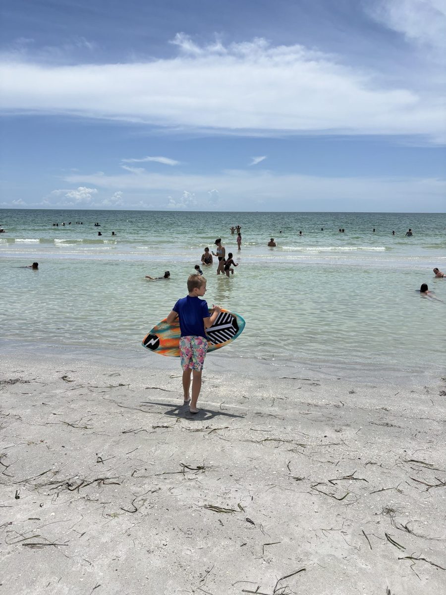 A boy carrying a skimboard through shallow water on Longboat Key.