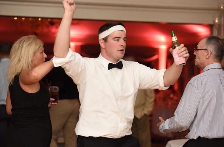 David McMahon in a bow tie and white headband dancing at a wedding reception.